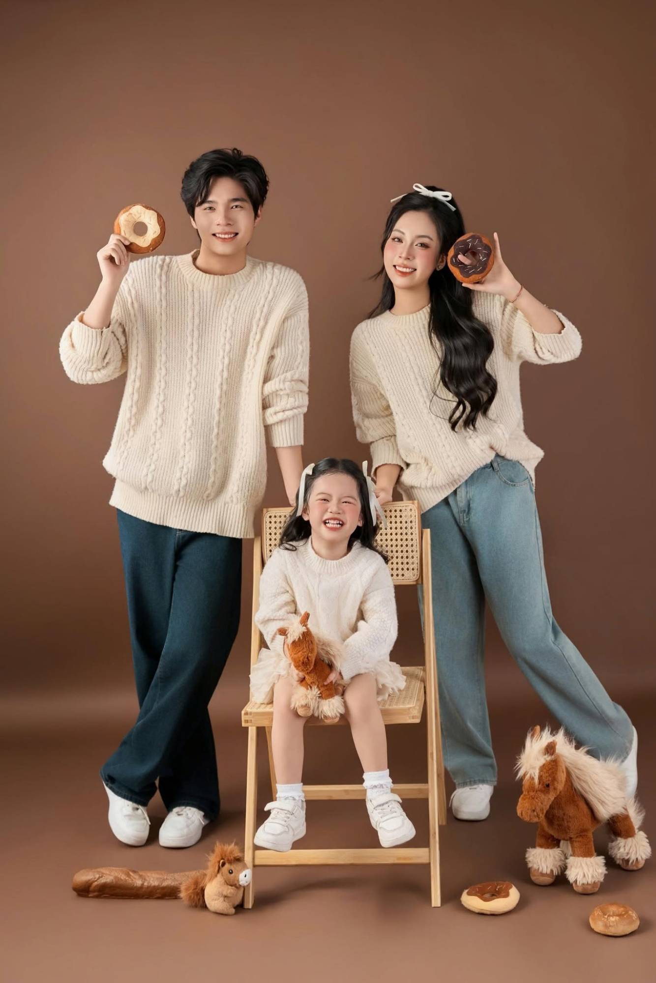 Bé gái cười ngồi ghế mây, bố mẹ cầm bánh donut