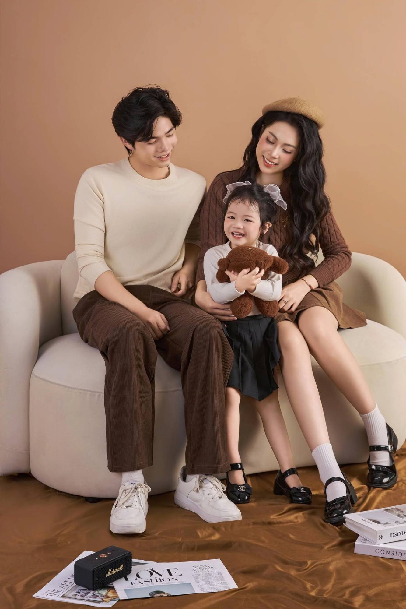 Gia đình mặc tông nâu be, bé gái ôm gấu bông